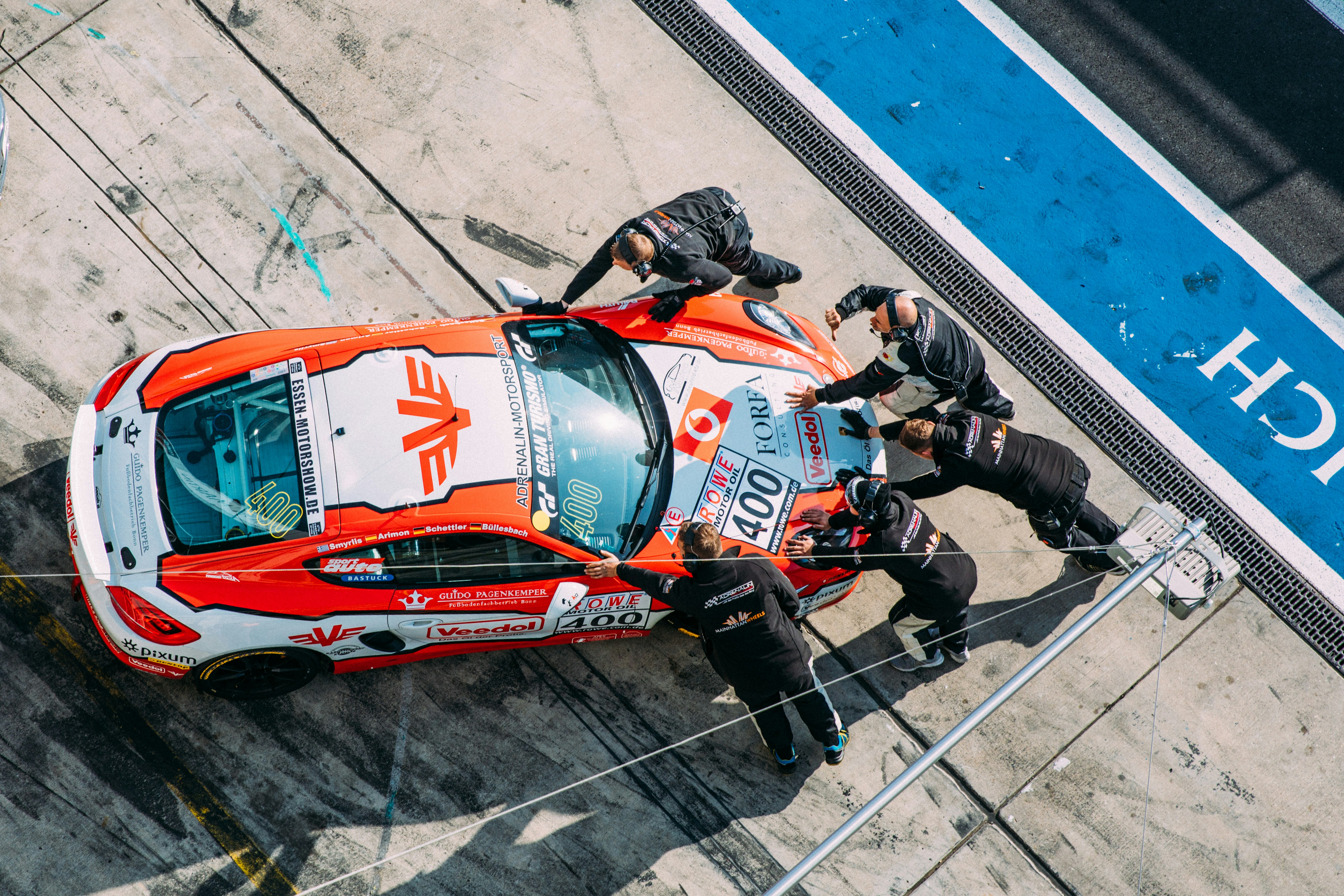 five men standing and pushing white and orange racing car on road